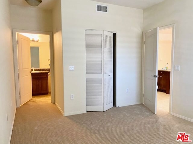 unfurnished bedroom with light carpet, ensuite bathroom, and a closet