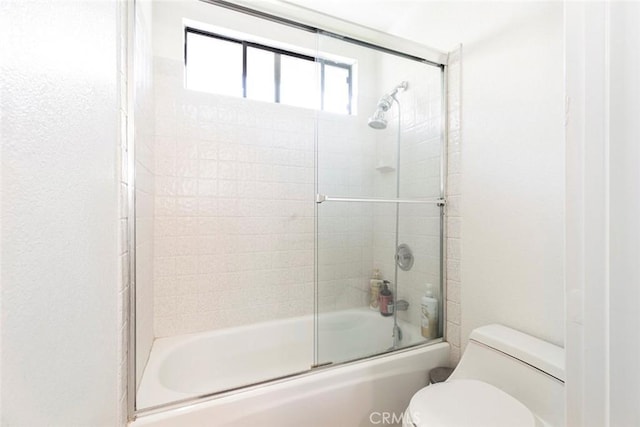 bathroom with toilet and shower / bath combination with glass door