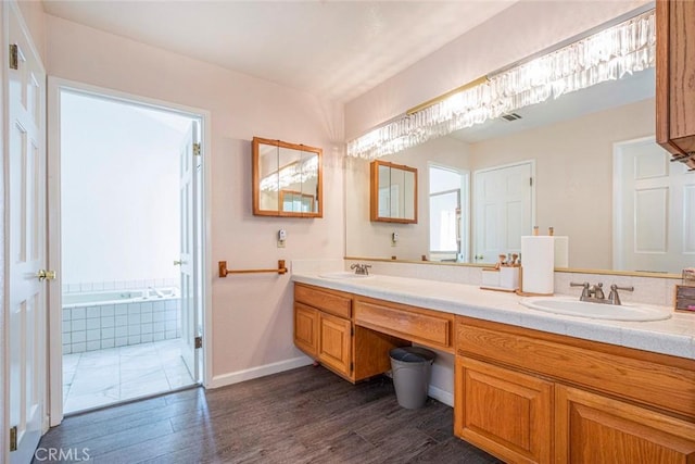 bathroom with wood-type flooring, vanity, and tiled tub