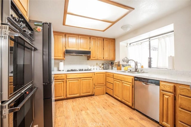 kitchen with sink, tasteful backsplash, stainless steel appliances, and light hardwood / wood-style flooring