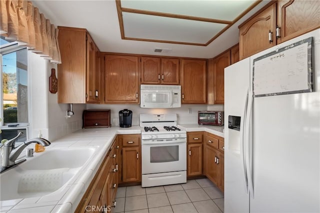 kitchen featuring tile counters, light tile patterned floors, sink, and white appliances