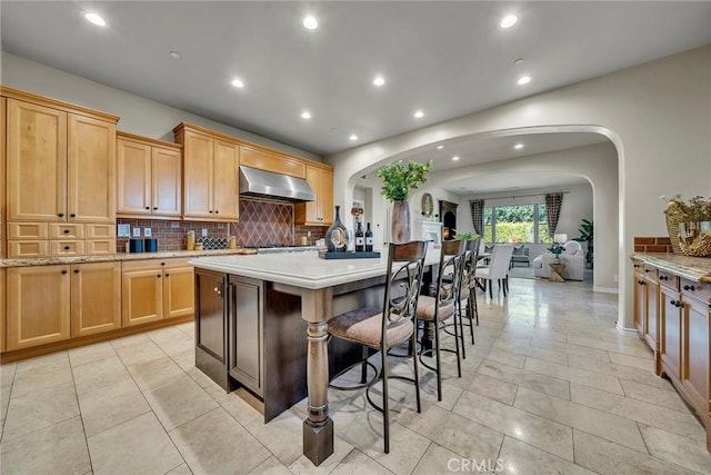 kitchen featuring decorative backsplash, light brown cabinetry, a kitchen bar, exhaust hood, and a kitchen island