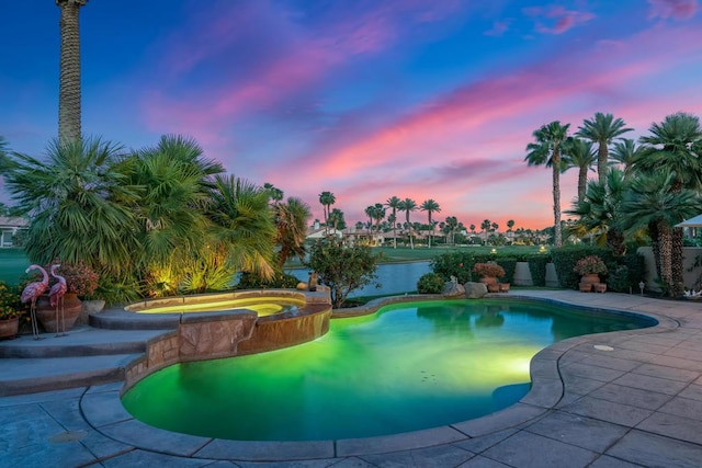 pool at dusk with an in ground hot tub and a patio area