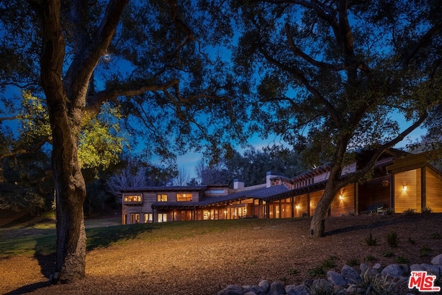 back house at dusk featuring a lawn