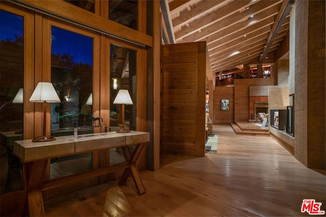 hallway featuring beam ceiling, wood walls, light hardwood / wood-style flooring, and french doors