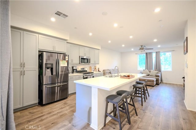 kitchen featuring sink, light wood-type flooring, an island with sink, appliances with stainless steel finishes, and a kitchen bar