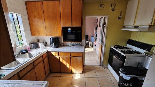 kitchen featuring sink, tile counters, range with gas stovetop, and light tile patterned flooring