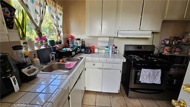 kitchen featuring light tile patterned floors, white cabinetry, stainless steel gas range oven, tile counters, and sink