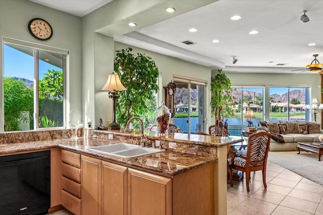 kitchen featuring ceiling fan, dishwasher, sink, dark stone counters, and light tile patterned floors