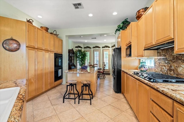 kitchen with a kitchen breakfast bar, light stone counters, black appliances, a kitchen island, and light tile patterned flooring