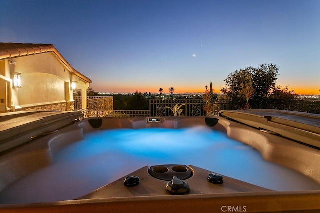 pool at dusk featuring a jacuzzi