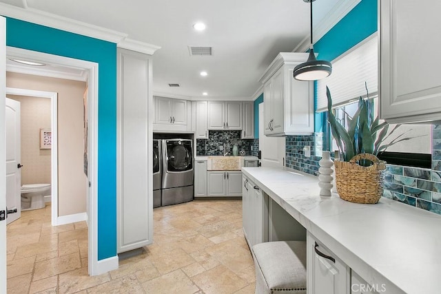 kitchen featuring tasteful backsplash, washing machine and dryer, light stone counters, pendant lighting, and ornamental molding