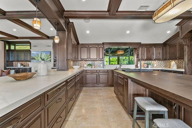 kitchen featuring hanging light fixtures, decorative backsplash, dark brown cabinets, beam ceiling, and a breakfast bar area