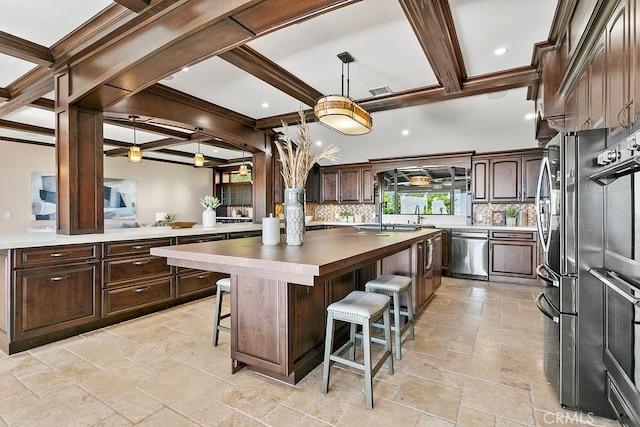 kitchen featuring dark brown cabinetry, a kitchen bar, decorative backsplash, a kitchen island, and appliances with stainless steel finishes