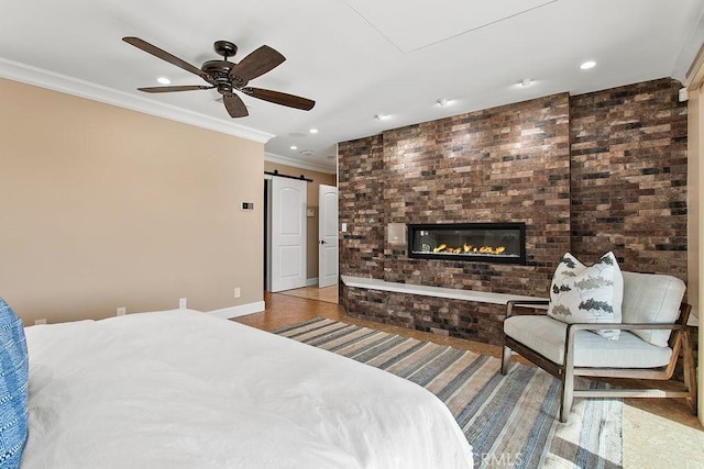 bedroom featuring a barn door, ceiling fan, crown molding, and a fireplace