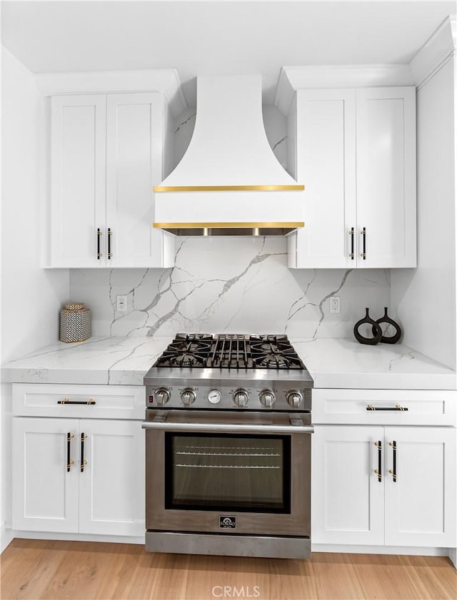 kitchen featuring light stone countertops, custom exhaust hood, light hardwood / wood-style flooring, high end stainless steel range, and white cabinets