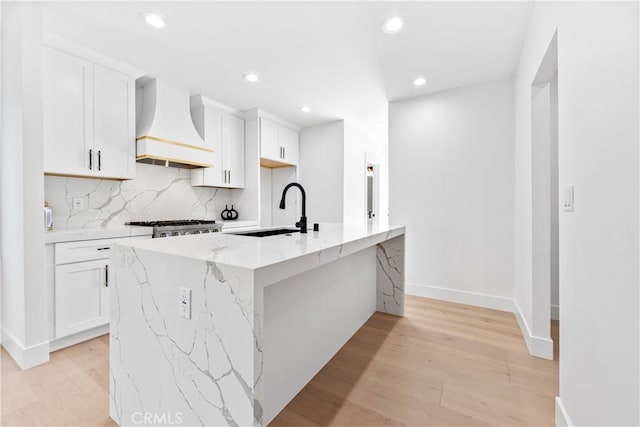 kitchen with sink, a center island with sink, white cabinetry, and custom exhaust hood