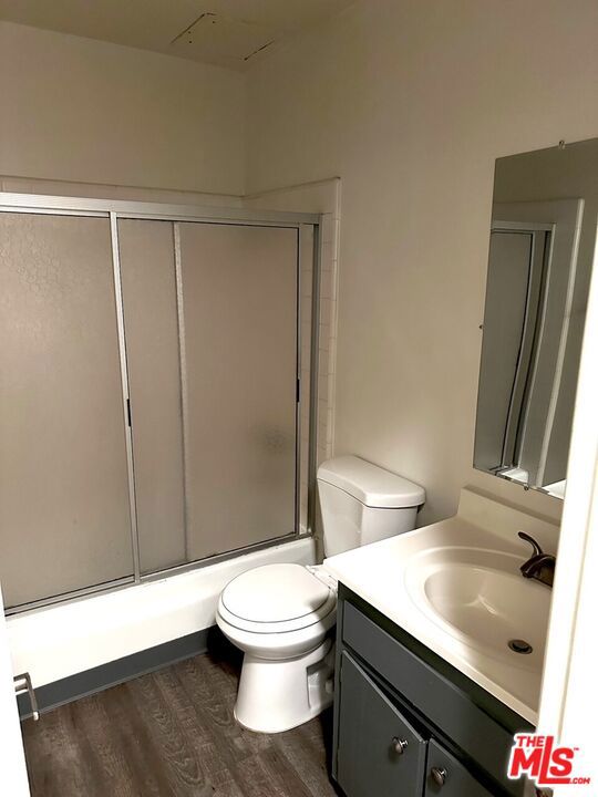 full bathroom with shower / bath combination with glass door, hardwood / wood-style floors, vanity, and toilet