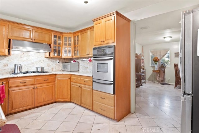 kitchen featuring decorative backsplash, light stone counters, light tile patterned floors, and appliances with stainless steel finishes