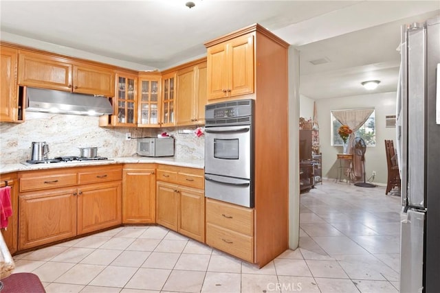 kitchen featuring appliances with stainless steel finishes, backsplash, light stone counters, and light tile patterned floors