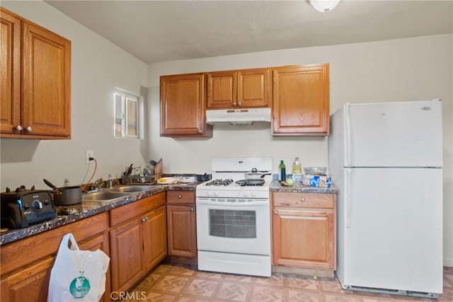 kitchen with white appliances, dark stone countertops, and sink