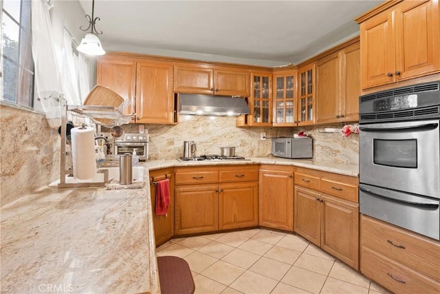 kitchen with appliances with stainless steel finishes, light stone counters, pendant lighting, backsplash, and light tile patterned floors