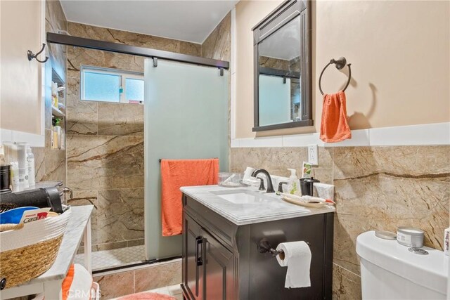 bathroom with a shower with door, vanity, tile walls, and toilet