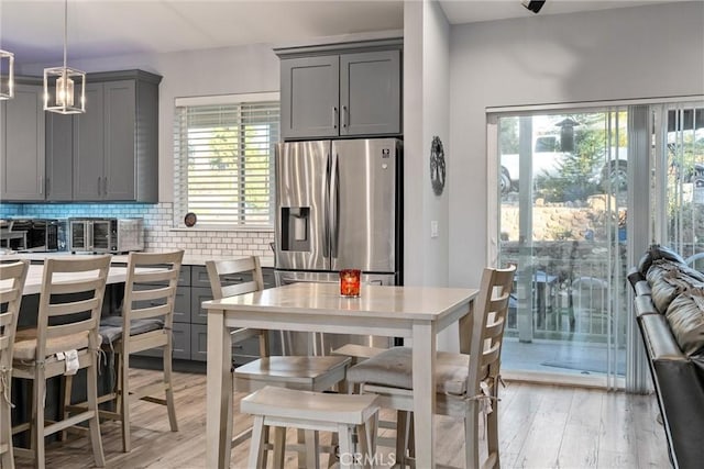 kitchen with gray cabinetry, decorative light fixtures, stainless steel refrigerator with ice dispenser, and light hardwood / wood-style flooring