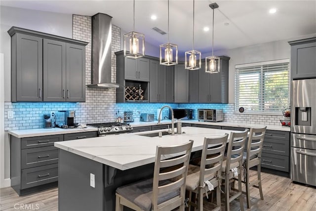 kitchen featuring appliances with stainless steel finishes, wall chimney range hood, decorative light fixtures, a breakfast bar area, and an island with sink