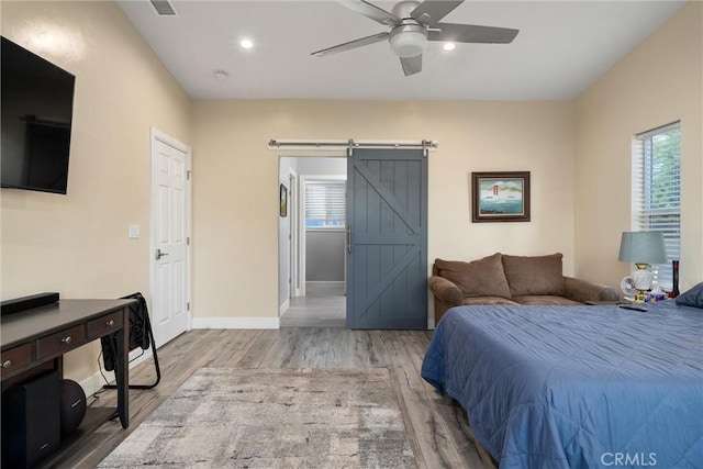 bedroom featuring ceiling fan, a barn door, light wood-type flooring, and multiple windows