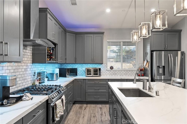 kitchen featuring sink, stainless steel appliances, light stone counters, pendant lighting, and light wood-type flooring