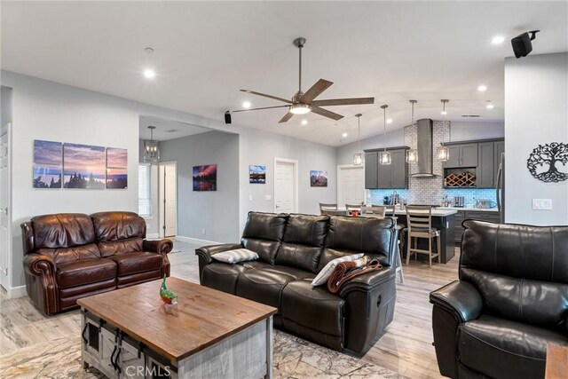 living room featuring ceiling fan with notable chandelier, light wood-type flooring, and vaulted ceiling