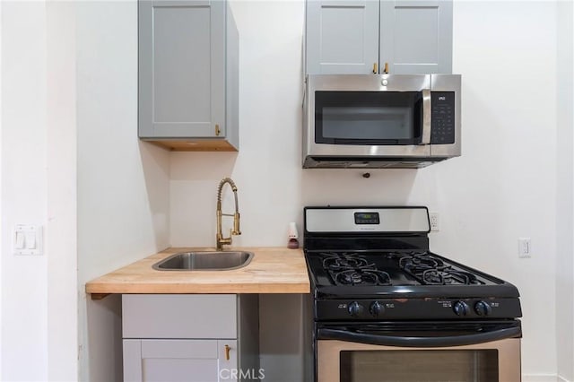 kitchen featuring gray cabinets, butcher block counters, gas range oven, and sink