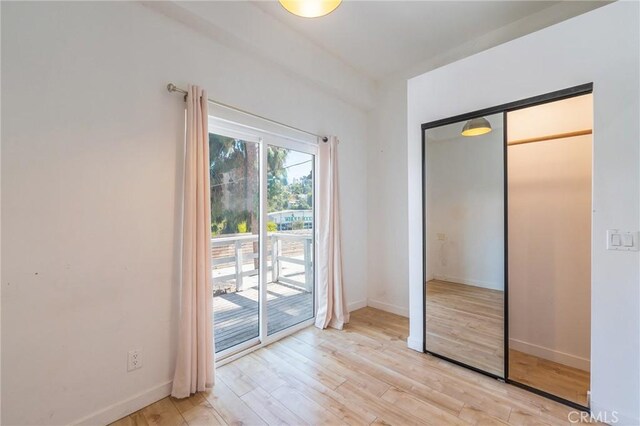 unfurnished bedroom featuring light wood-type flooring, access to outside, and a closet