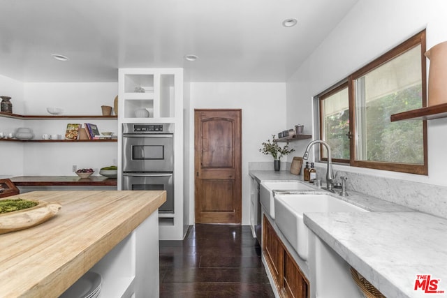 kitchen with double oven, light stone counters, sink, and dark wood-type flooring