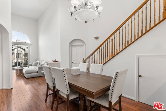 dining area with a towering ceiling, dark wood-type flooring, and an inviting chandelier