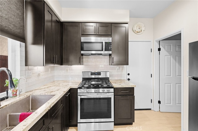 kitchen with appliances with stainless steel finishes, light wood-type flooring, tasteful backsplash, dark brown cabinets, and sink