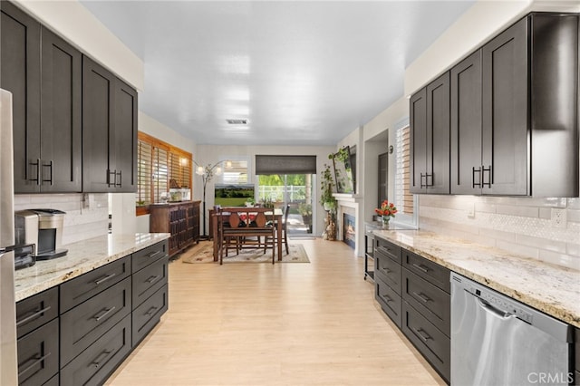 kitchen featuring tasteful backsplash, light stone counters, stainless steel dishwasher, and light wood-type flooring