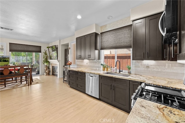 kitchen featuring sink, decorative backsplash, light wood-type flooring, appliances with stainless steel finishes, and dark brown cabinetry