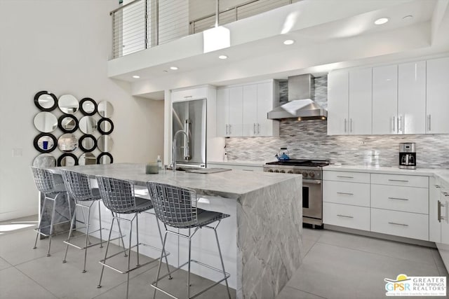 kitchen with a breakfast bar area, an island with sink, wall chimney range hood, and premium appliances