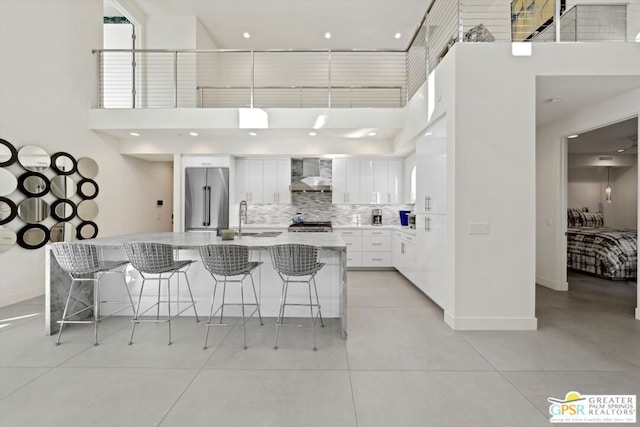 kitchen with a breakfast bar area, wall chimney exhaust hood, an island with sink, white cabinetry, and stainless steel appliances