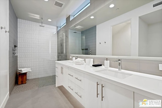 bathroom with a tile shower, vanity, concrete floors, and tile walls