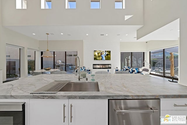 kitchen with a towering ceiling, light stone counters, a large fireplace, decorative light fixtures, and white cabinetry