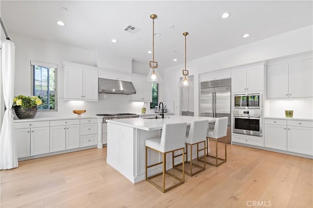 kitchen featuring built in appliances, decorative light fixtures, and white cabinets