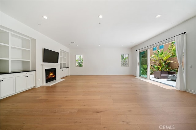 66 Poncho, Irvine, CA 92602 - unfurnished living room with light wood-style flooring, built in shelves, recessed lighting, and a lit fireplace