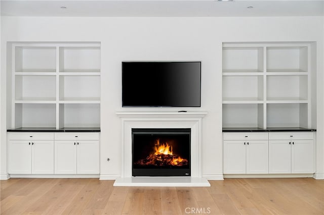 66 Poncho, Irvine, CA 92602 - unfurnished living room with light wood-style floors, a warm lit fireplace, and built in shelves