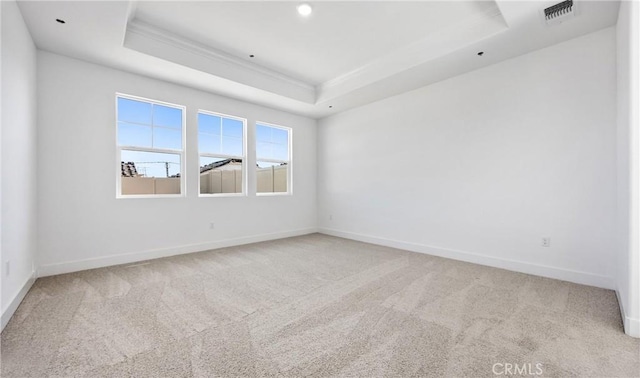 spare room featuring light colored carpet, a raised ceiling, visible vents, and baseboards