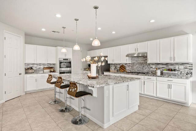 kitchen with pendant lighting, white cabinets, light tile patterned floors, stainless steel appliances, and a center island with sink