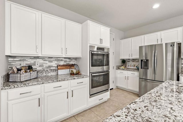 kitchen with light tile patterned floors, appliances with stainless steel finishes, white cabinetry, backsplash, and light stone counters