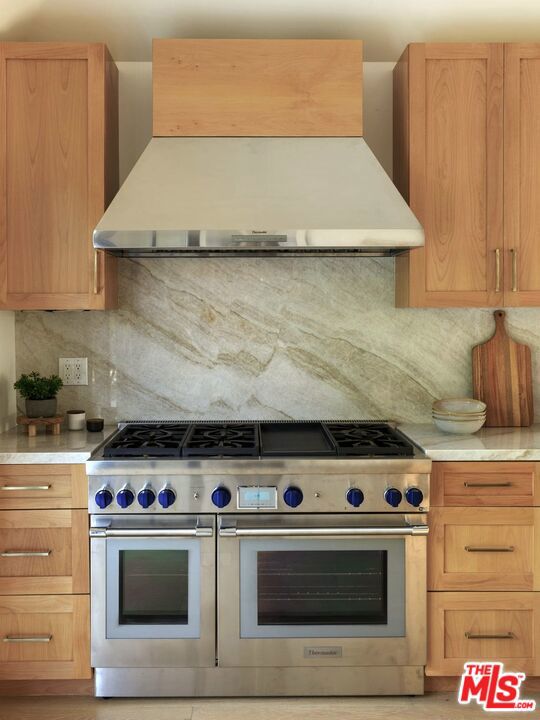 kitchen featuring backsplash, light brown cabinetry, wall chimney exhaust hood, and range with two ovens